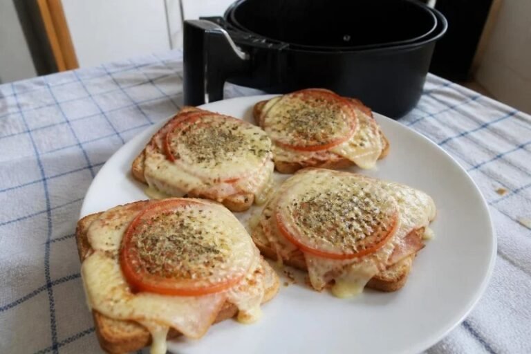 Mini pizzas de pão de forma feitas na air fryer, com muçarela derretida, presunto, tomate e orégano, num prato branco