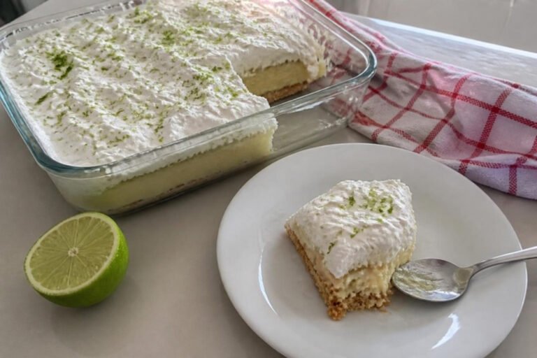 Torta de limão sem forno na travessa de vidro e uma fatia servida num pratinho, com meio limão ao lado